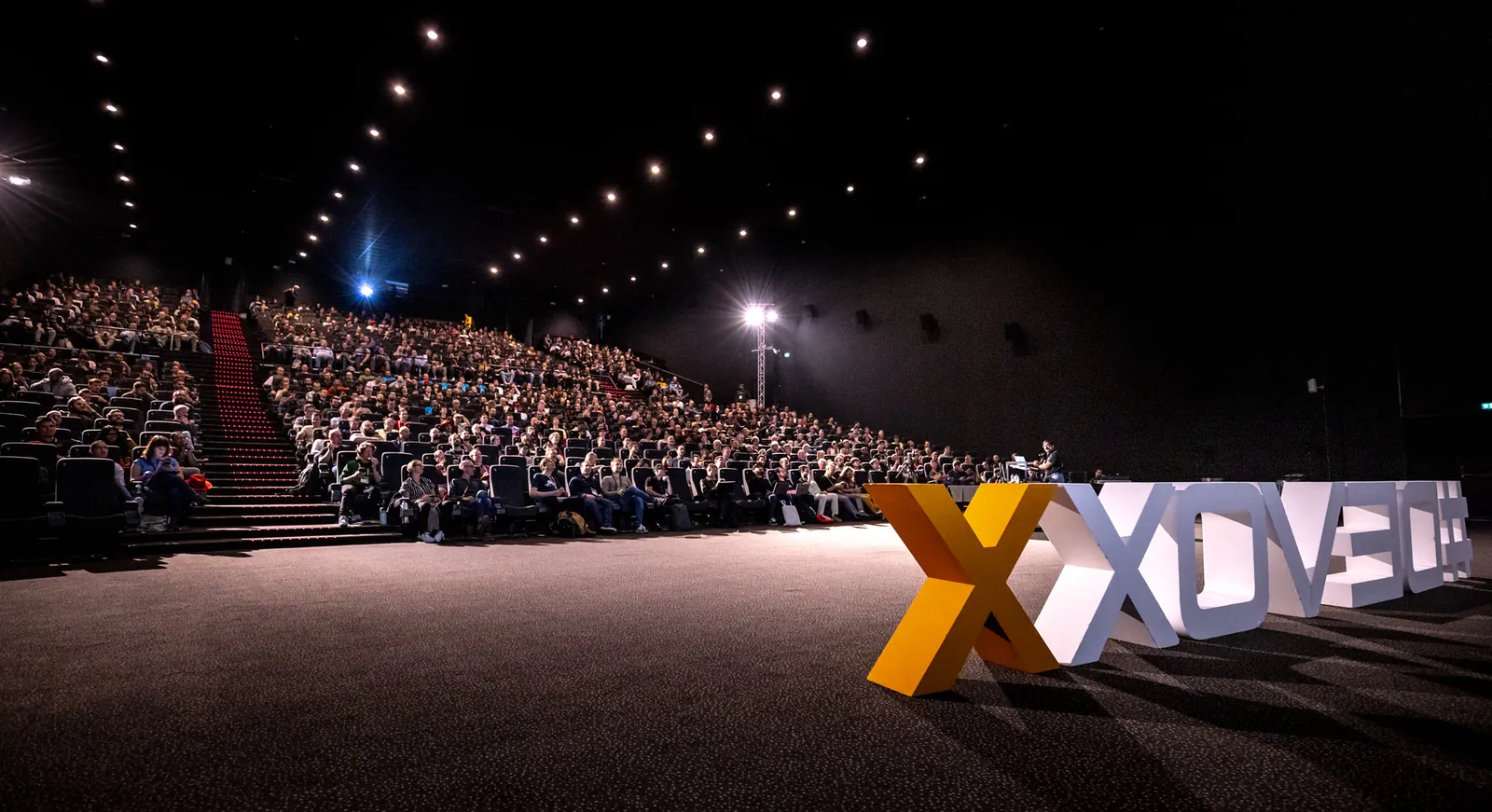A packed cinema room at Devoxx Belgium with the #DEVOXX letters on stage
